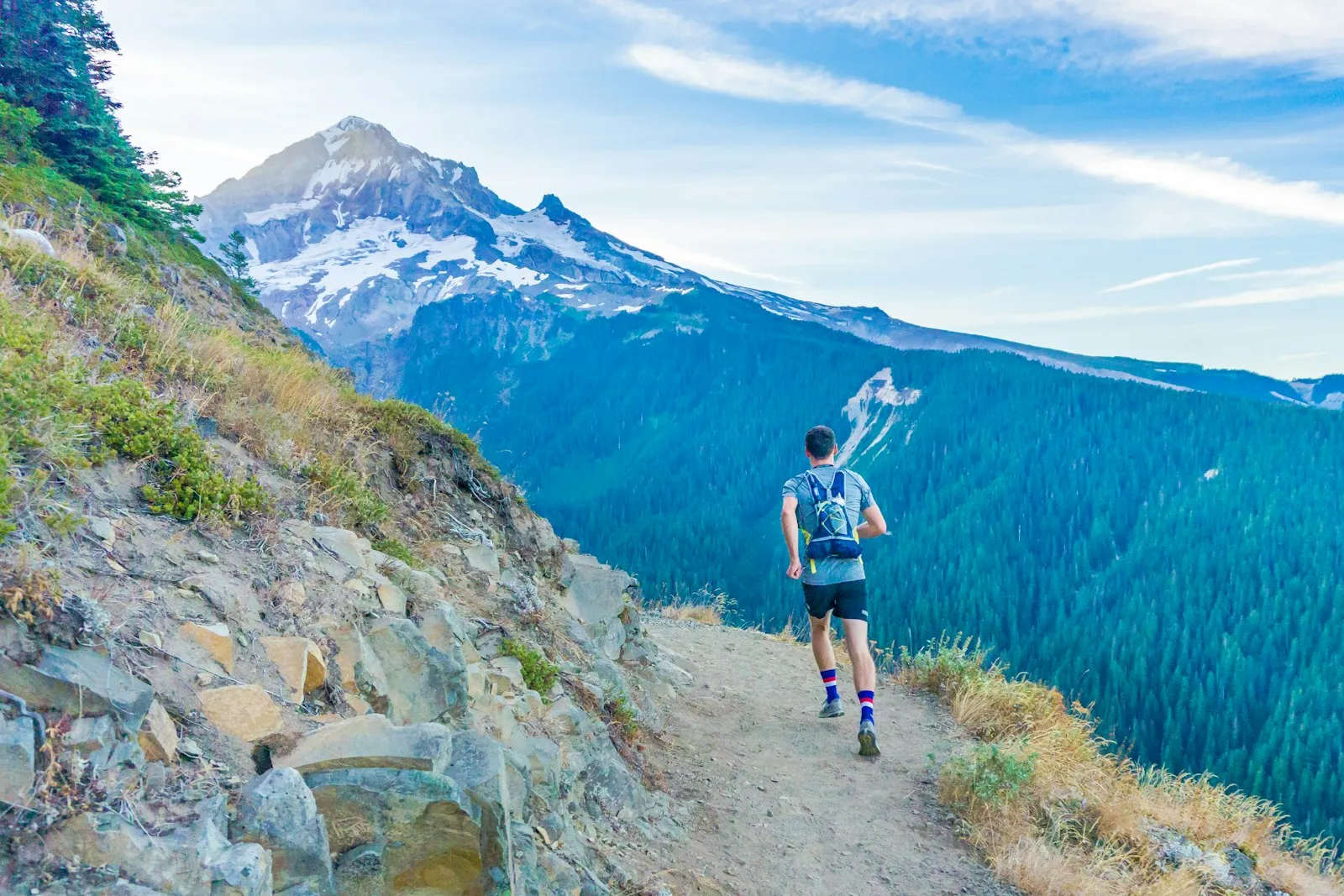 A trail runner climbing a mountain path toward a snow-capped peak