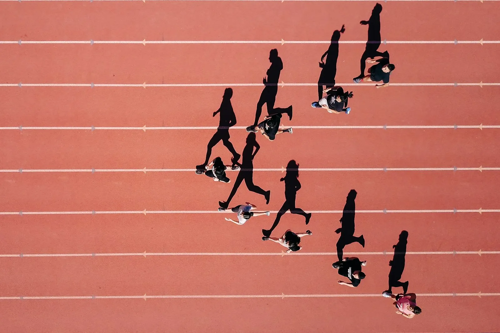 Overhead view of a dozen runners spread across the lanes of a red running track